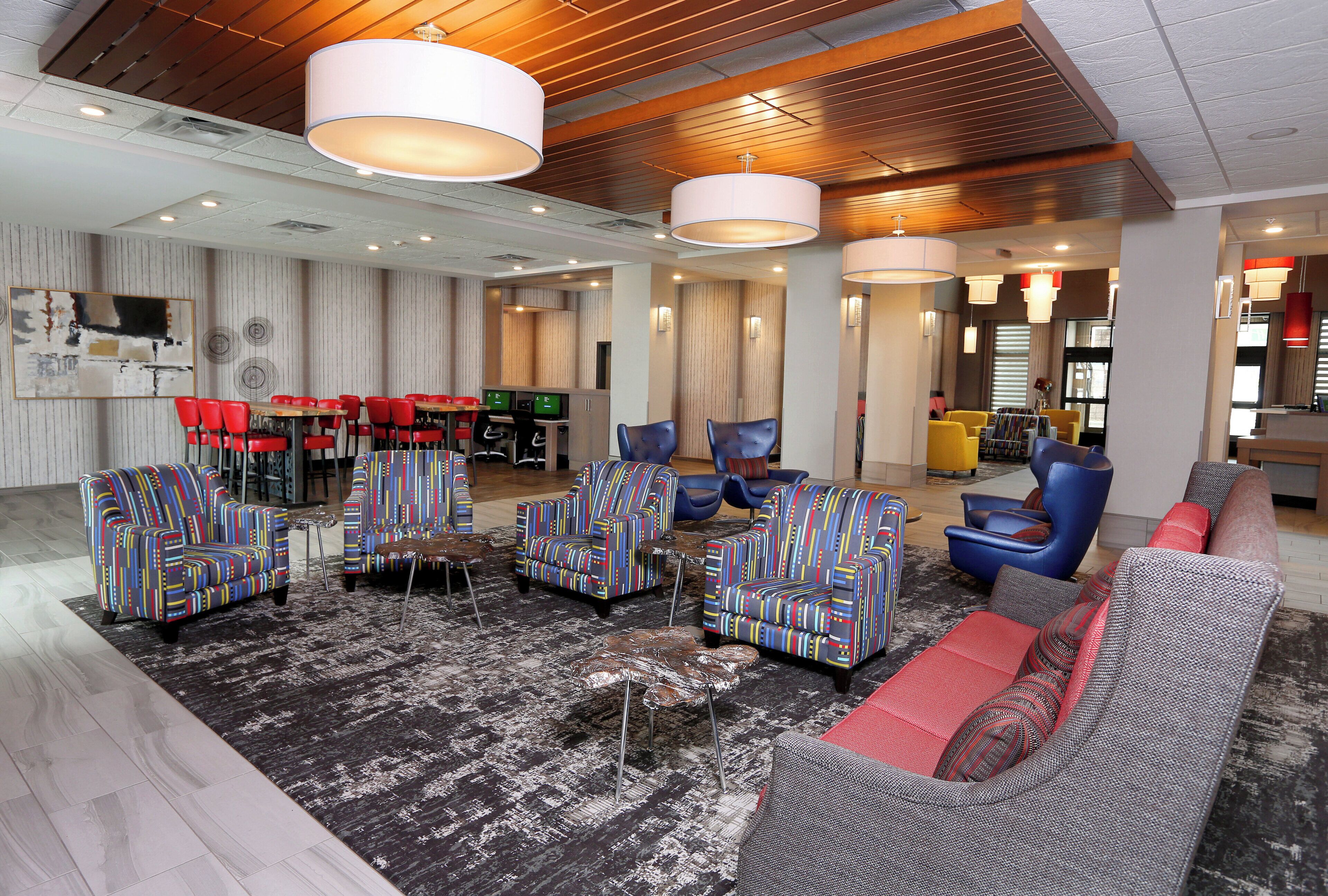Un hall d’hôtel moderne offrant différents types de sièges, notamment des canapés et des fauteuils, ainsi qu’un espace repas avec des chaises rouges.