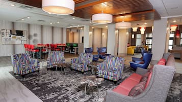 A modern hotel lobby with a mix of seating options, including sofas and armchairs, and a dining area with red chairs.