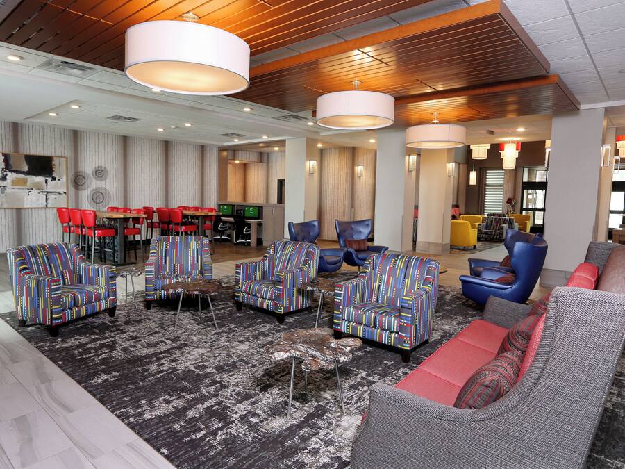 A modern hotel lobby with a mix of seating options, including sofas and armchairs, and a dining area with red chairs.