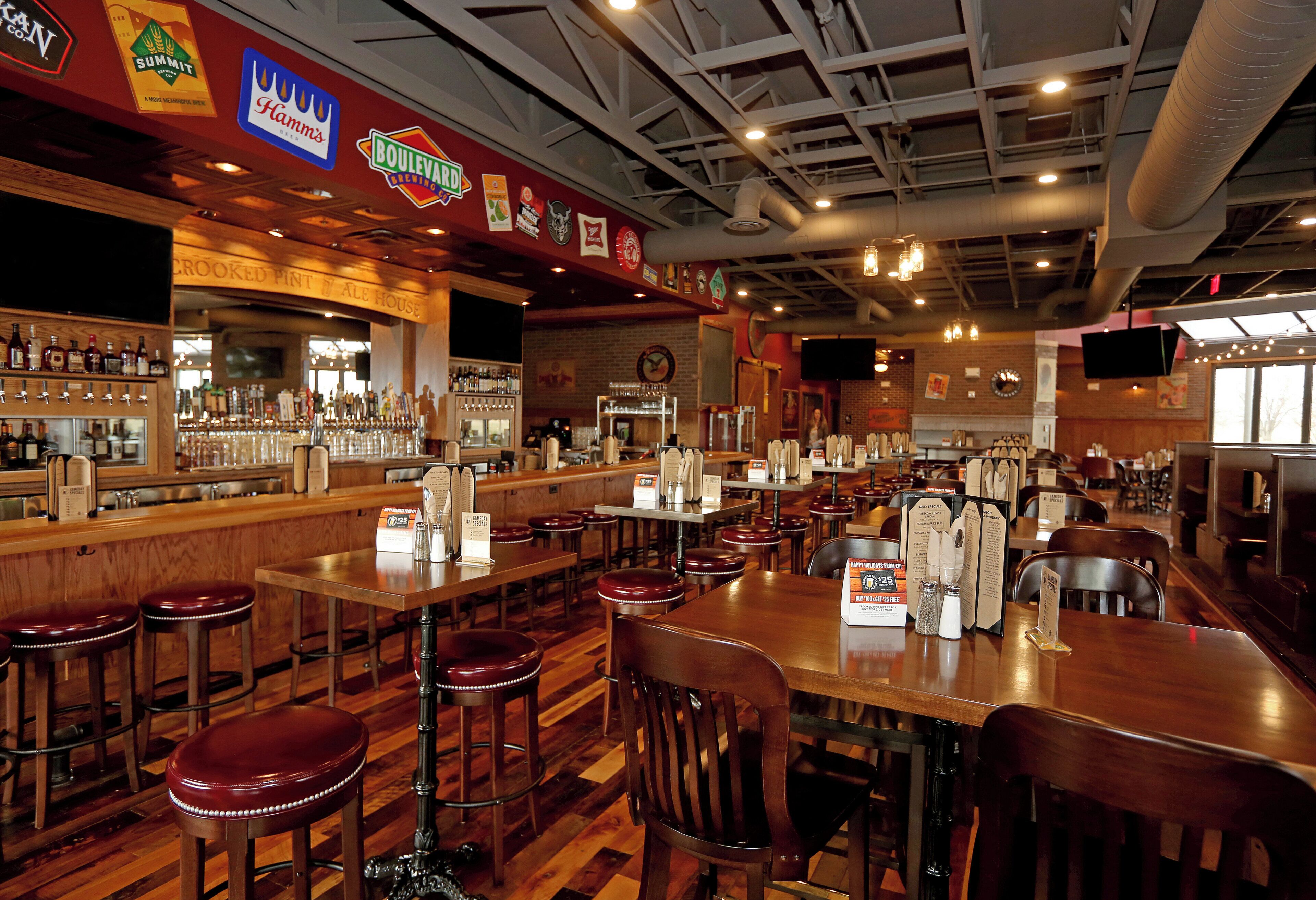 A bar area with multiple stools, a counter with various bottles, and signs for different beers.