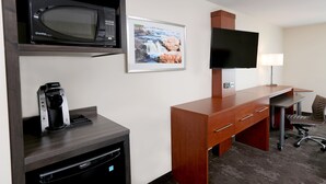 Une chambre d’hôtel équipée d’un four à micro-ondes, d’une machine à café, d’une télévision, d’un bureau, d’une chaise et d’un tableau encadré au mur.