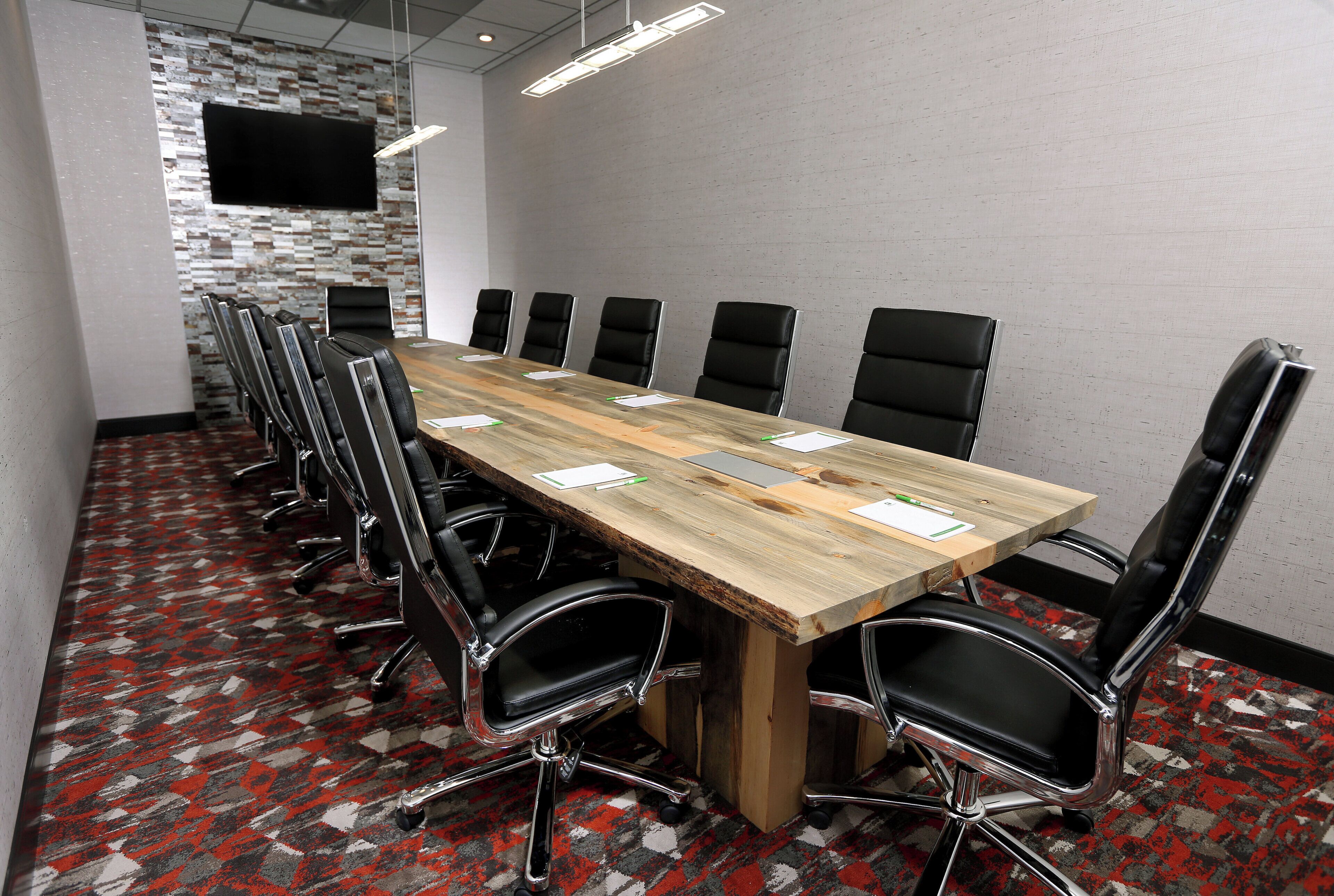 A conference room with a long table, black chairs, and a flat-screen TV on the wall.