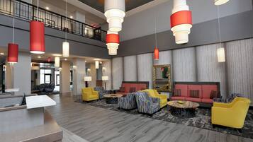 A spacious lobby with multiple seating areas, a reception desk, and a staircase leading to an upper level.