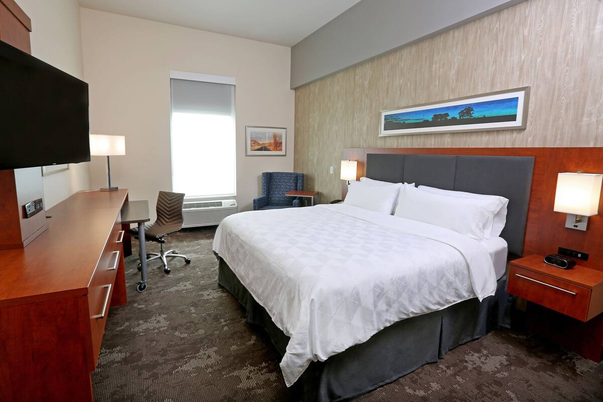 Une chambre d’hôtel avec un grand lit, un bureau, une chaise, une télévision et un tableau au mur.