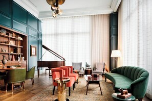 A spacious living room with a grand piano, a green sofa, and a variety of chairs.