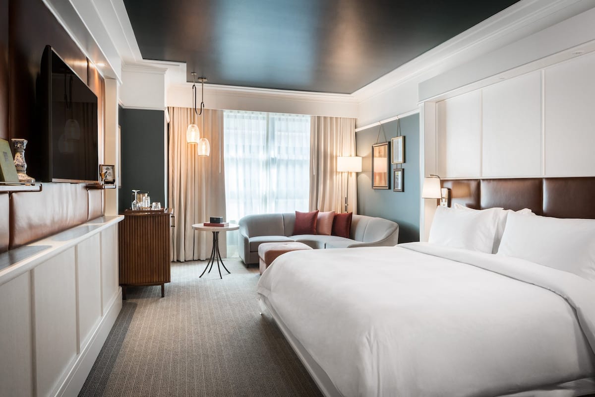 A hotel room with a large bed, a sofa, a small table, and a TV.