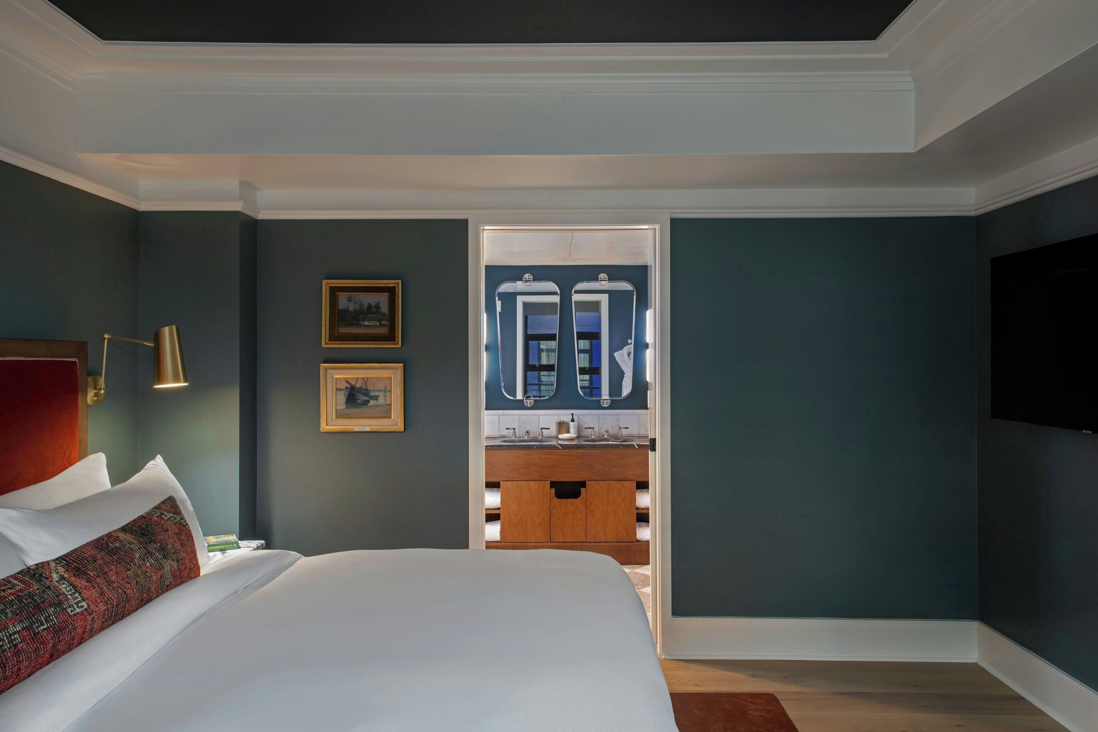 Ein Hotelzimmer mit einem großen Bett, einem hölzernen Schminktisch, einem Spiegel und einem an der Wand befestigten Fernseher.