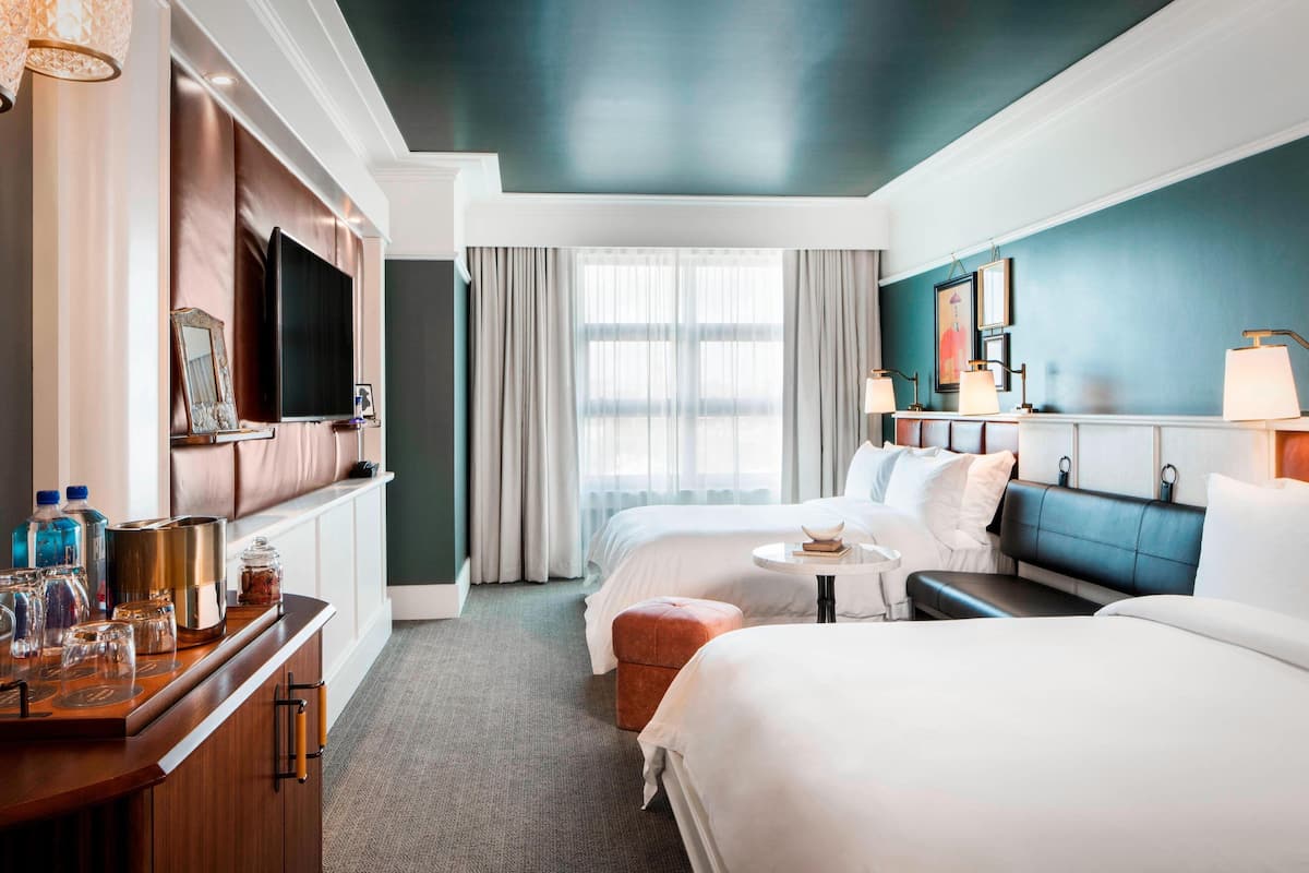 A hotel room with a large bed, a smaller bed, a sofa, a TV, a minibar, and a window with curtains.