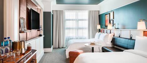 Hotelkamer met een groot bed, een kleiner bed, een bank, een televisie, een minibar en een raam met gordijnen.