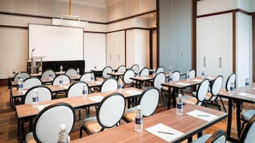 A conference room with multiple tables, chairs, and a large screen.