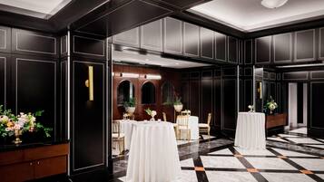 A spacious hotel lobby with a checkered marble floor, black paneling, and round tables with white tablecloths.