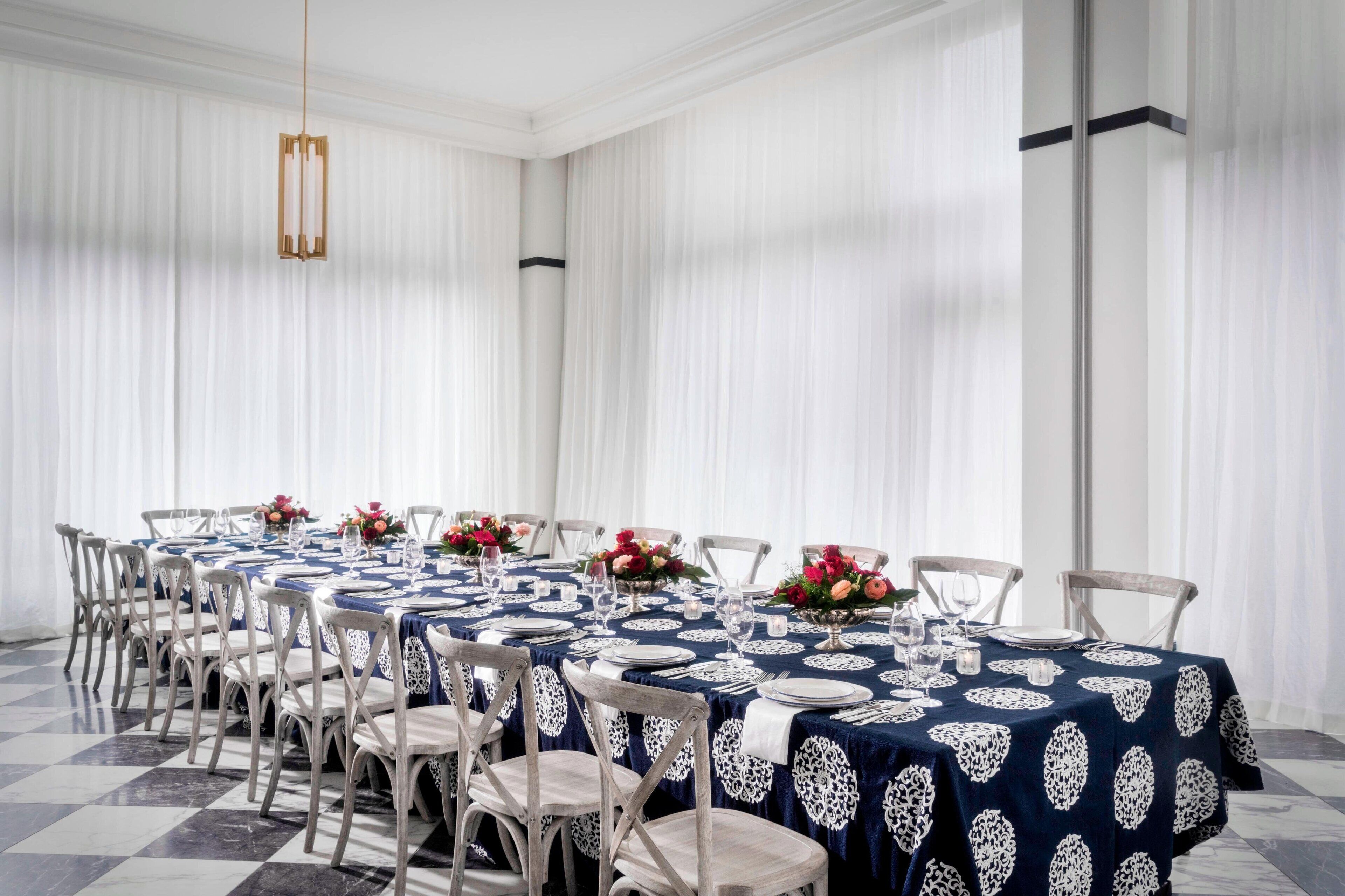 Un espace repas avec des tables rondes disposées pour accueillir six personnes, chacune étant recouverte d’une nappe en dentelle blanche et agrémentée d’un arrangement floral.