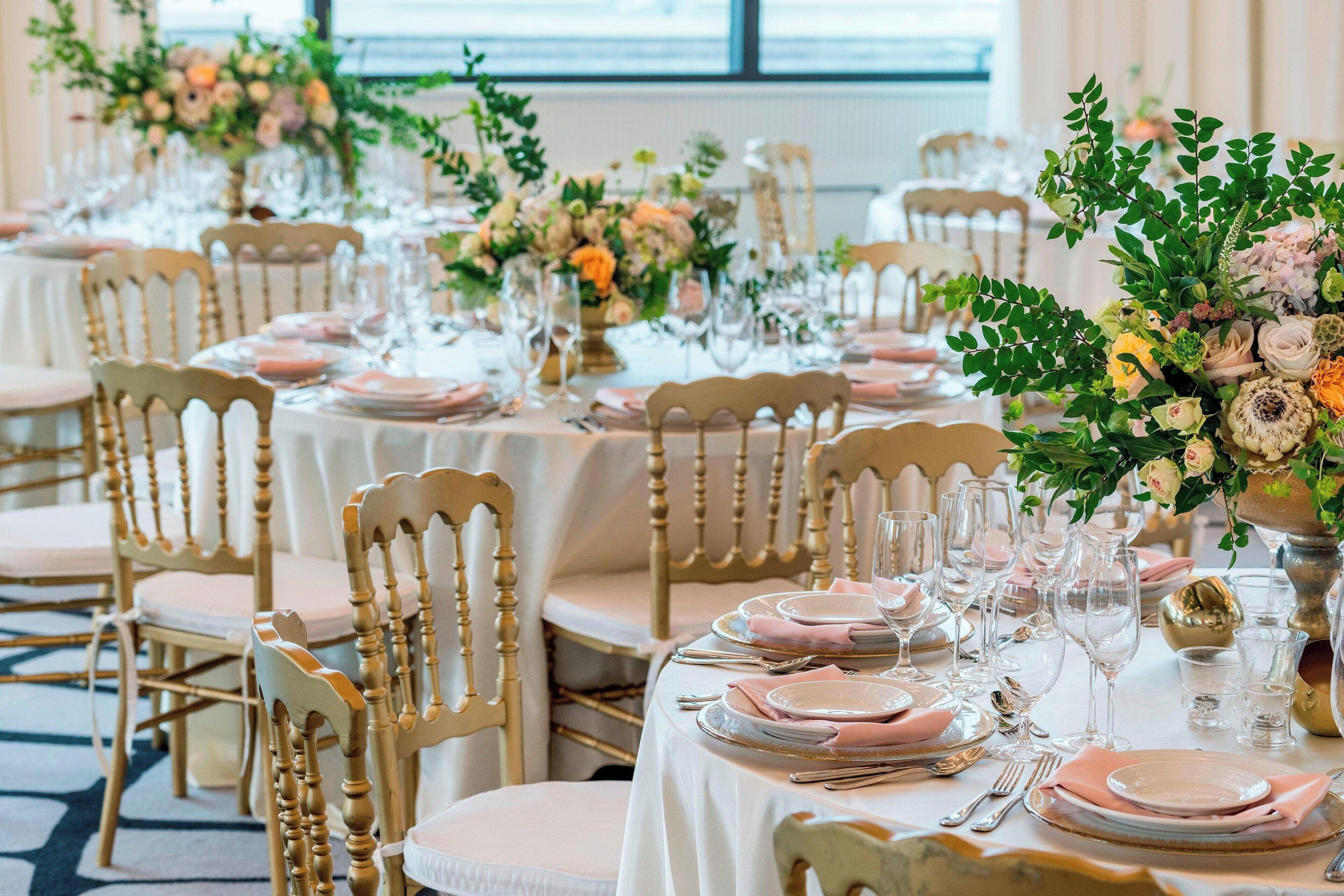 A banquet hall with round tables set for a formal event, featuring floral centerpieces and gold accents.