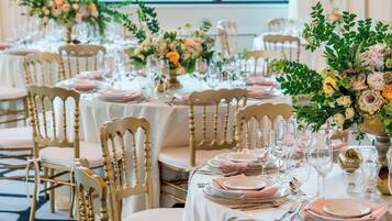 A banquet hall with round tables set for a formal event, featuring floral centerpieces and gold accents.