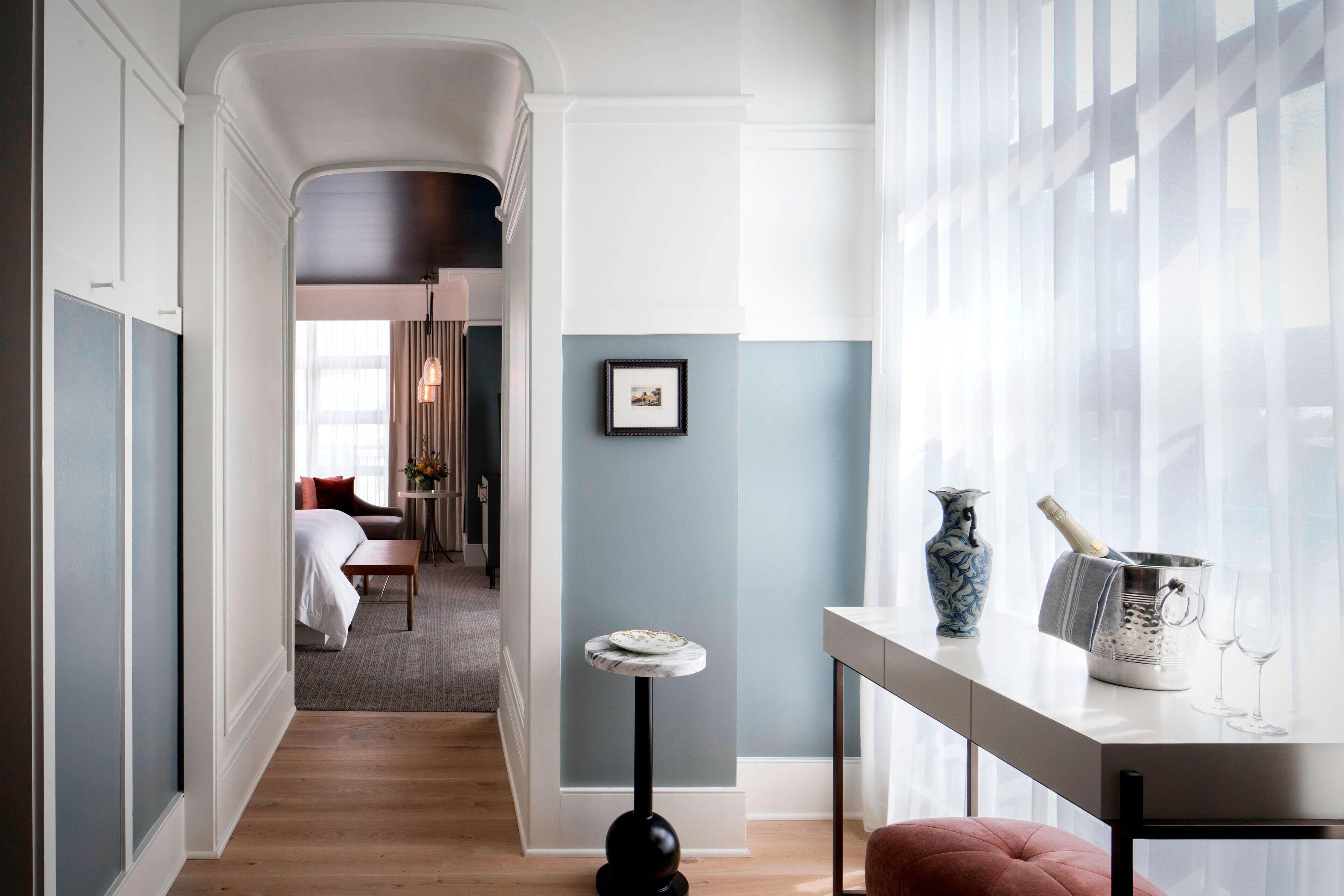 Ein Hotelzimmer mit Holzboden, einem weißen Bett, einem kleinen runden Tisch, einer Vase und einem Champagnerkühler.