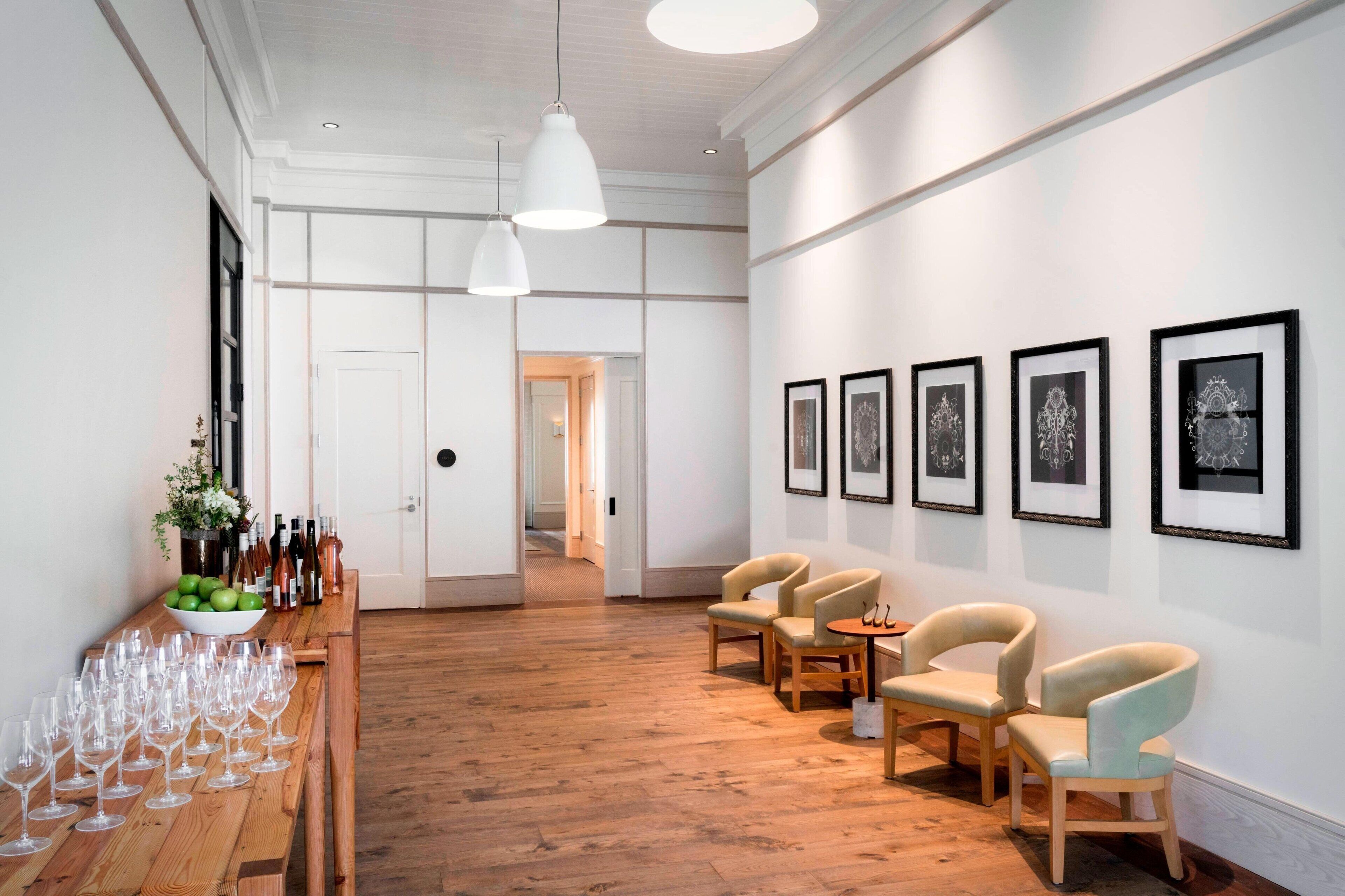 A spacious room with wooden flooring, a long table with wine glasses and bottles, and several chairs.