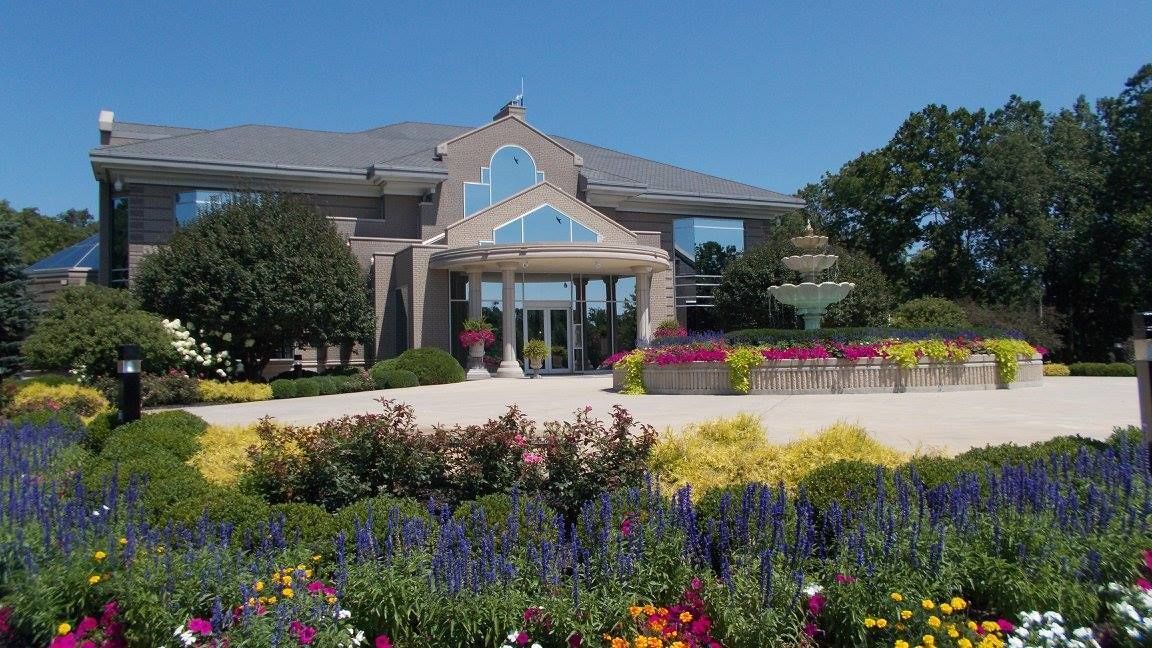 A modern building with a covered entrance, surrounded by a well-maintained garden with various colorful flowers and shrubs.