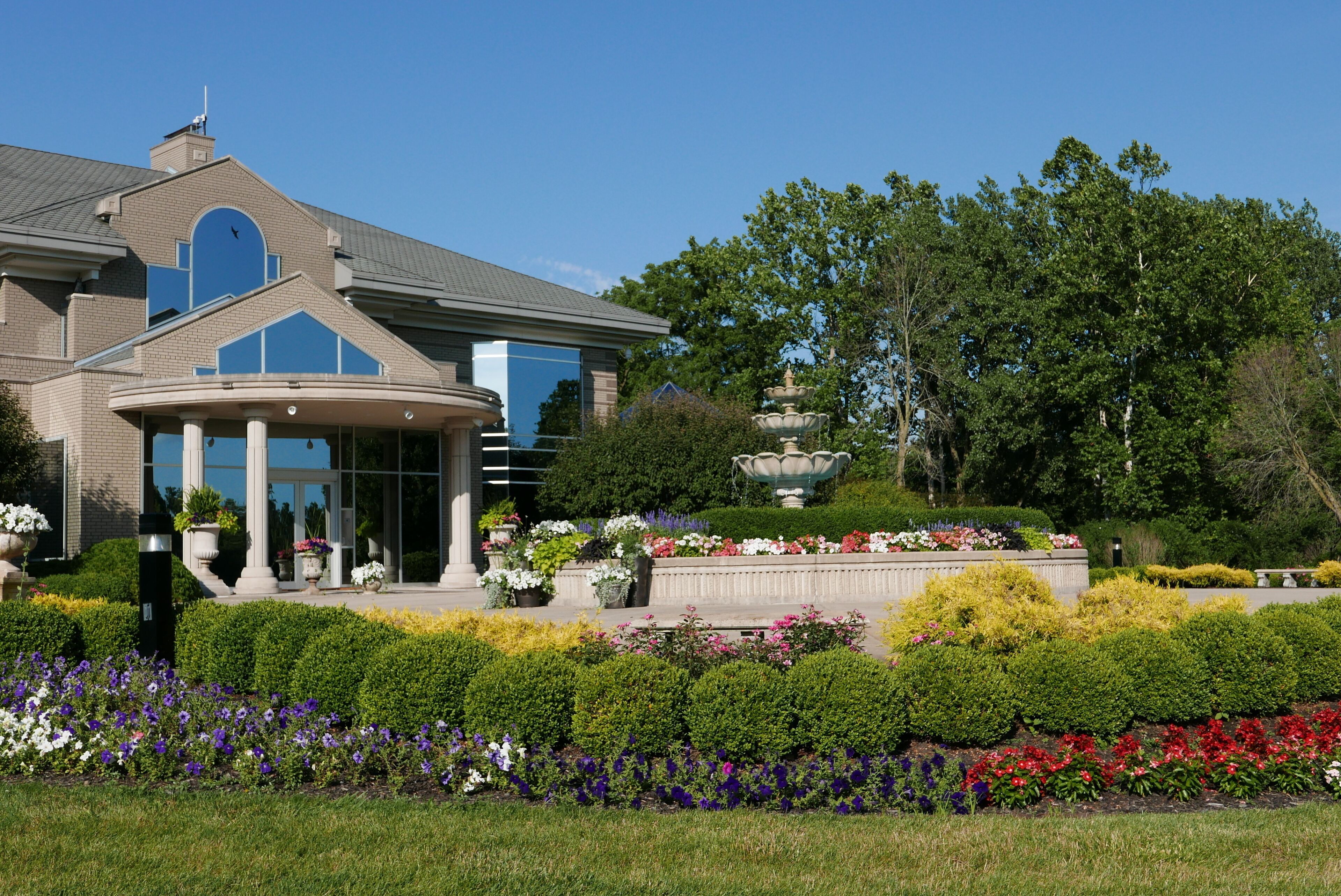 A large building with a central entrance, surrounded by well-maintained gardens and a fountain.