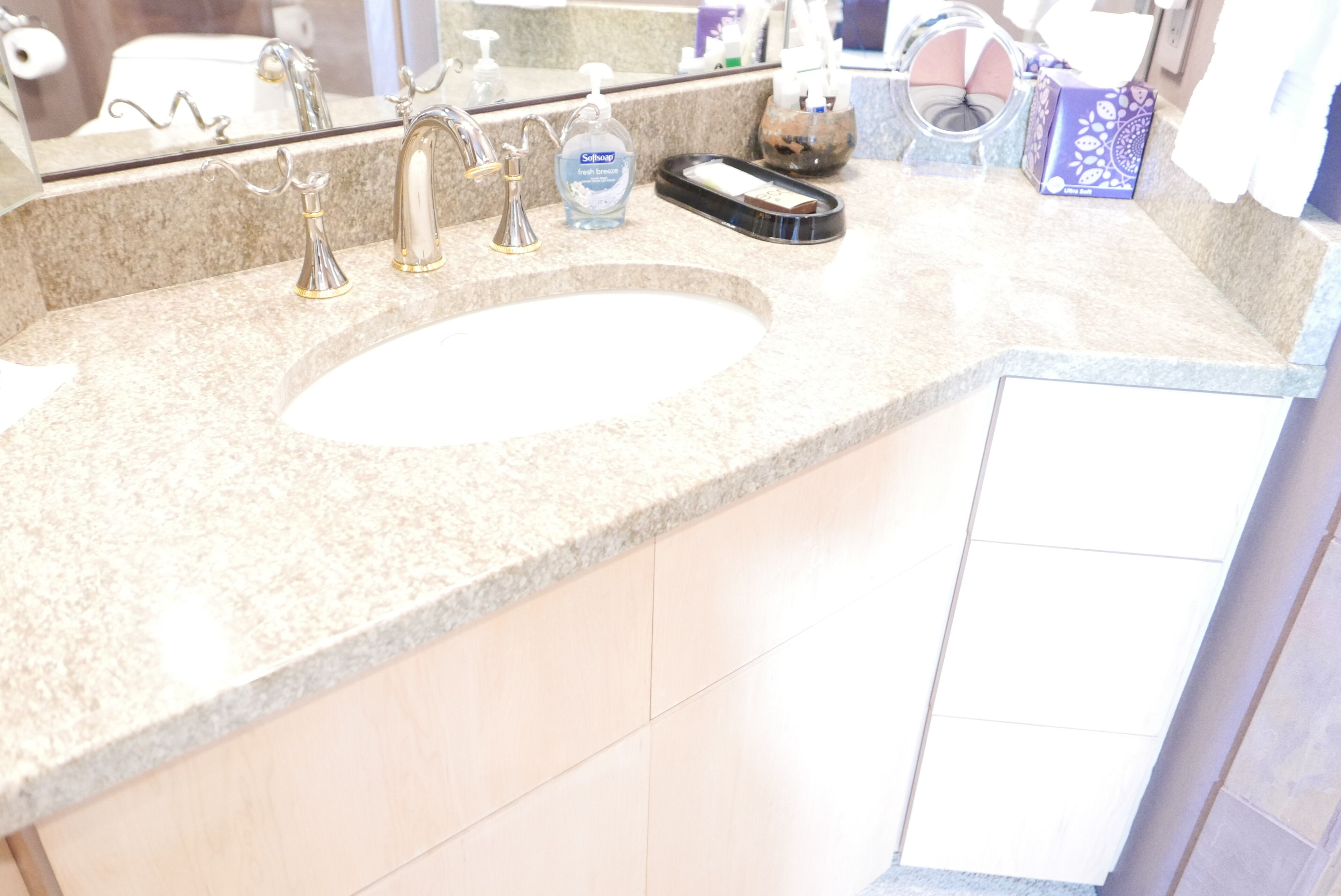 A bathroom with a granite countertop, a sink, a mirror, and toiletries.