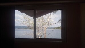 A window with a view of a body of water, a tree, and a distant shoreline. - Hotel Santa Bárbara Tikal (San Benito)