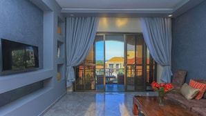 A modern living room with a flat-screen TV, a wooden coffee table, a sofa, and a sliding glass door leading to an outdoor patio. - Bon Bini Residence (Kampala)