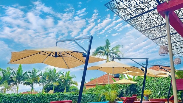 A poolside area with lounge chairs and umbrellas, surrounded by greenery and a clear sky. - Bon Bini Residence (Kampala)