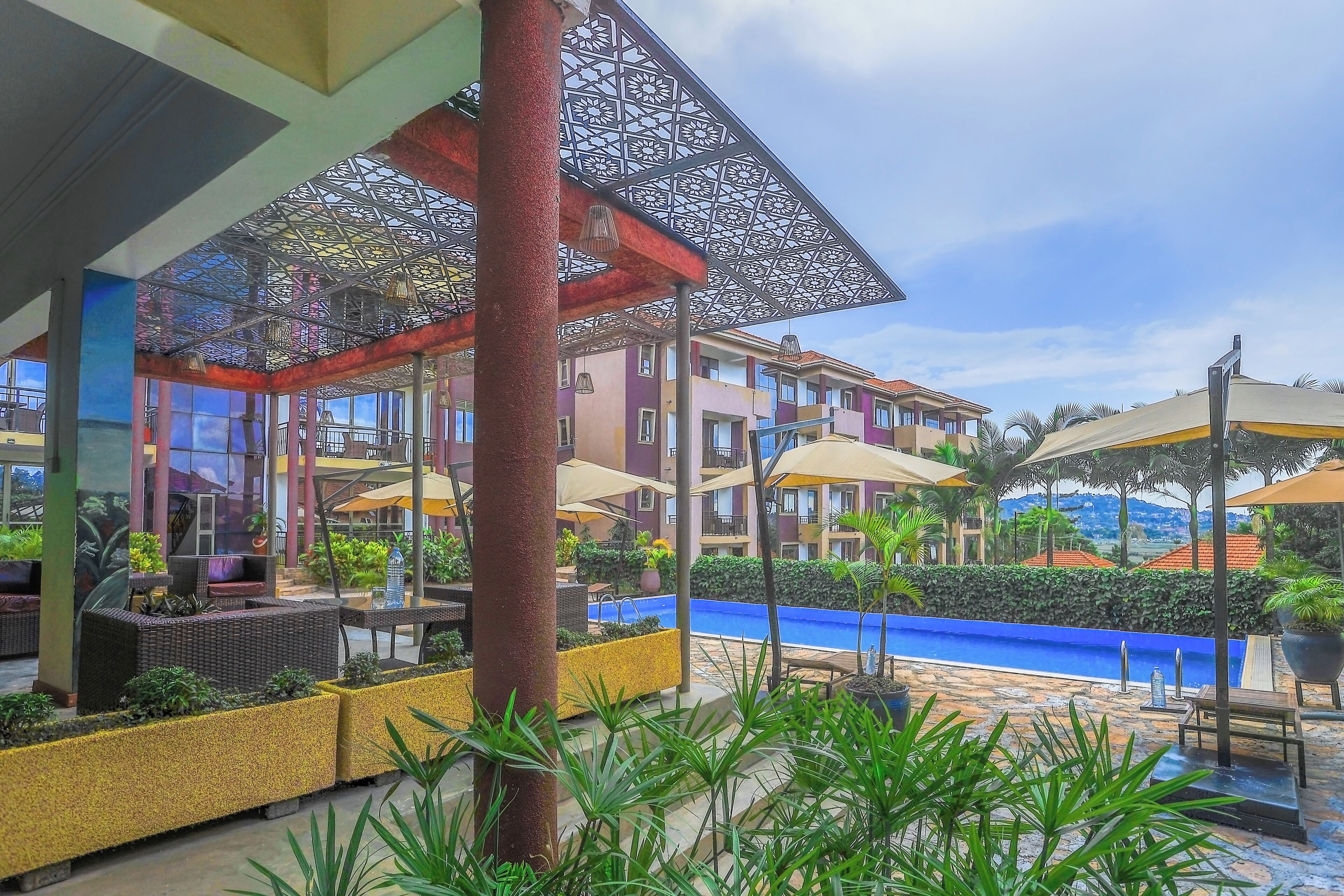A hotel courtyard with outdoor seating, a swimming pool, and multi-story buildings in the background.