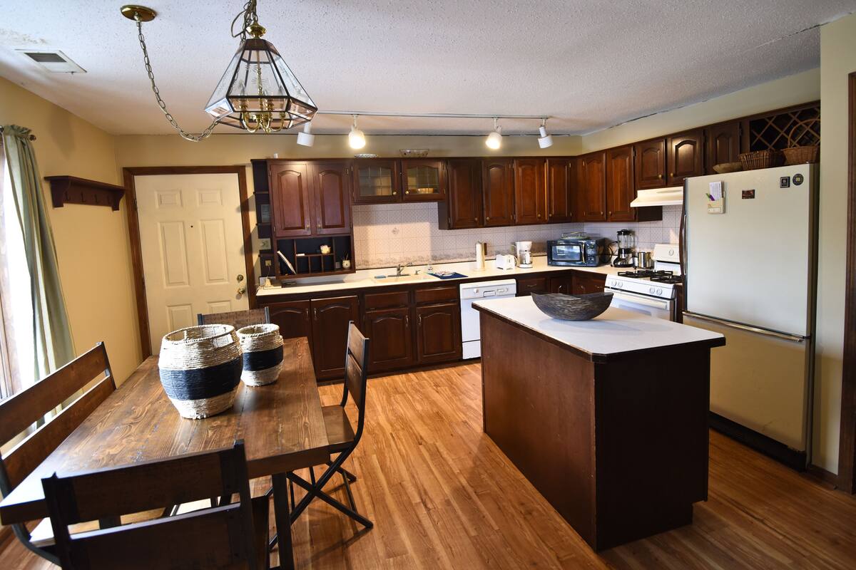 Una cocina con armarios de madera, una isla central, una mesa de comedor con sillas y una araña.