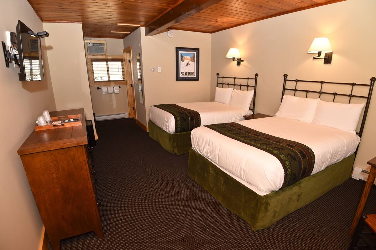 Habitación de hotel con dos camas, un escritorio de madera, un espejo y un cuadro en la pared.