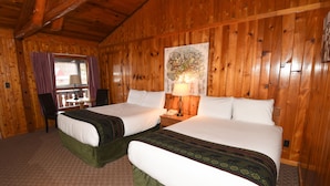 A wooden cabin room with two beds, a window with curtains, a table with a lamp, and a painting on the wall. - Timber Inn Motel (Ludlow)