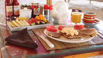 A breakfast table with various food items, a bottle of ketchup, a teapot, a jug of juice, and a cup.