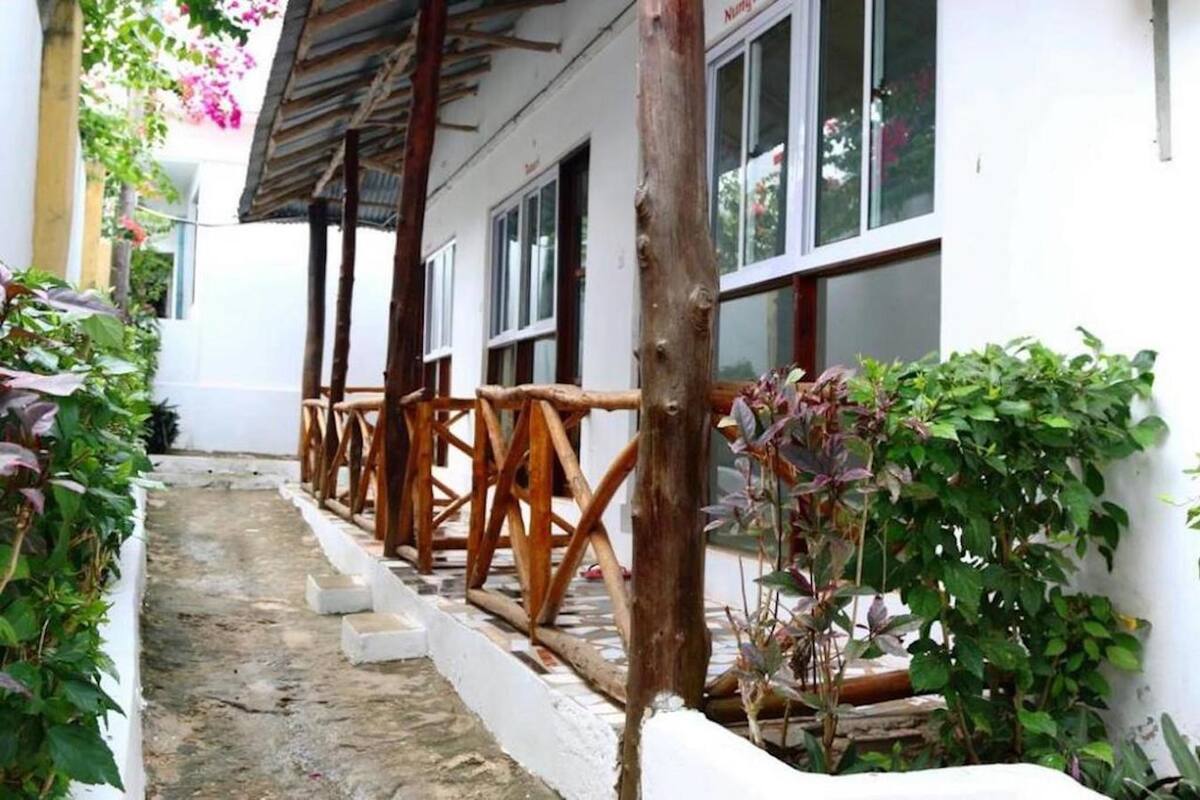 Un sendero estrecho que lleva a un edificio con un porche de madera y paredes blancas.