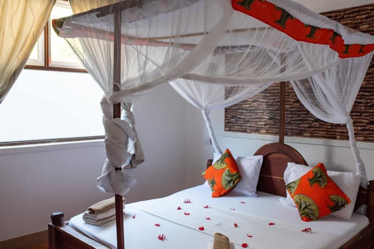 Una cama con dosel, almohadas y colcha con motivos florales rojos.