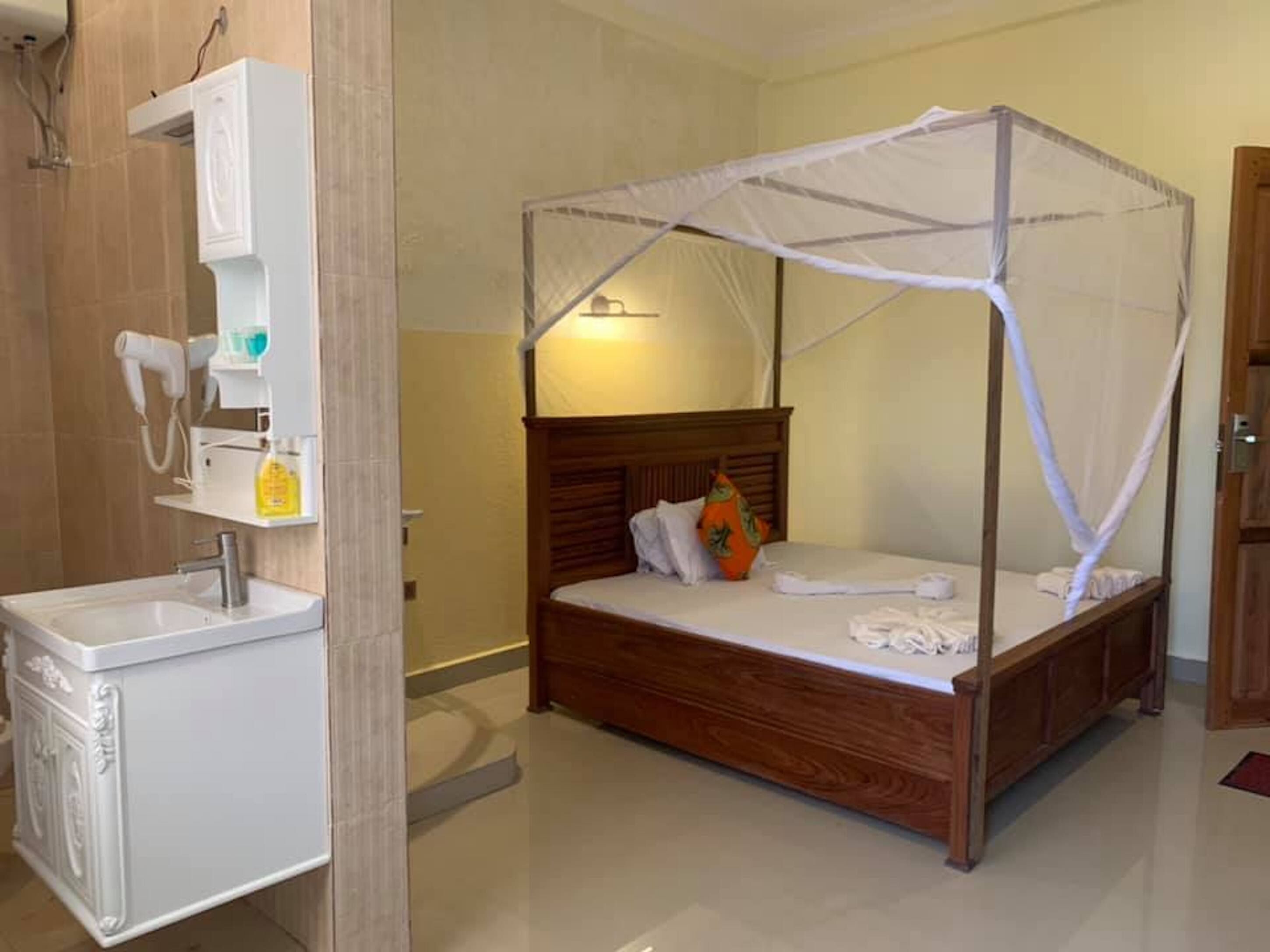 Un dormitorio con una cama de madera, dosel, mesita de noche y lavamanos integrado.