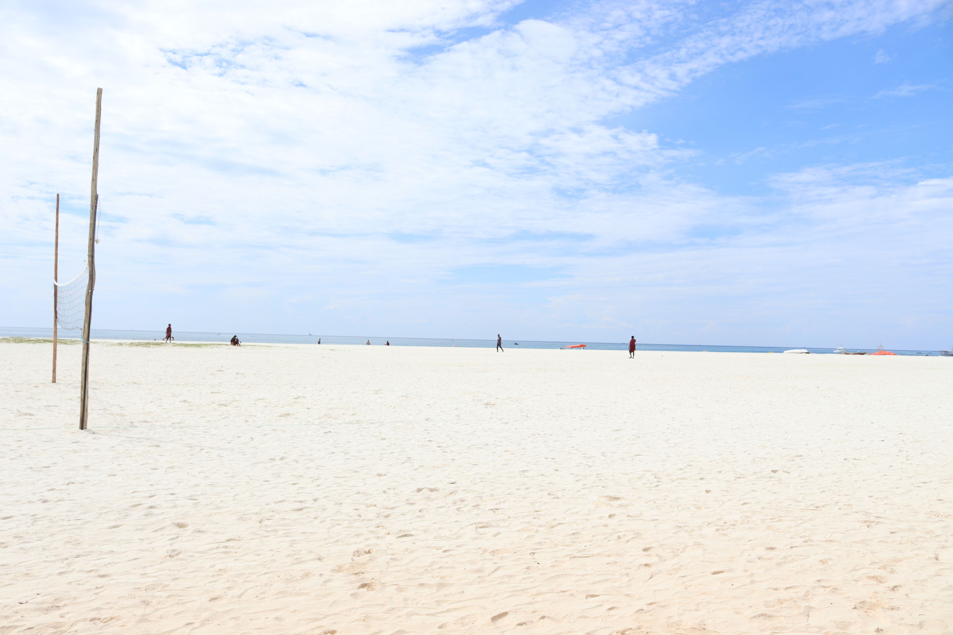 A sandy beach with a volleyball net and a few people in the distance.