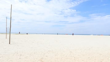 A sandy beach with a volleyball net and a few people in the distance.