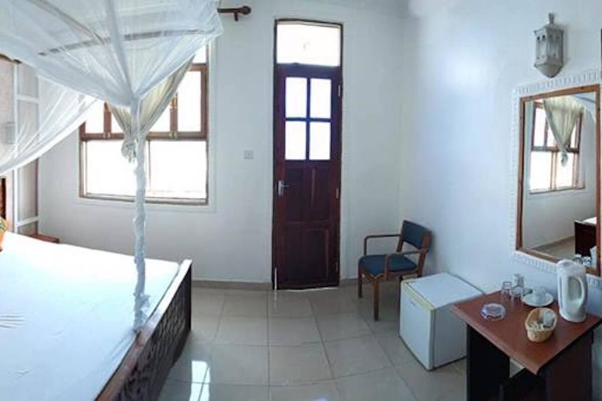 Un dormitorio con cama, escritorio, silla, puerta y ventana.