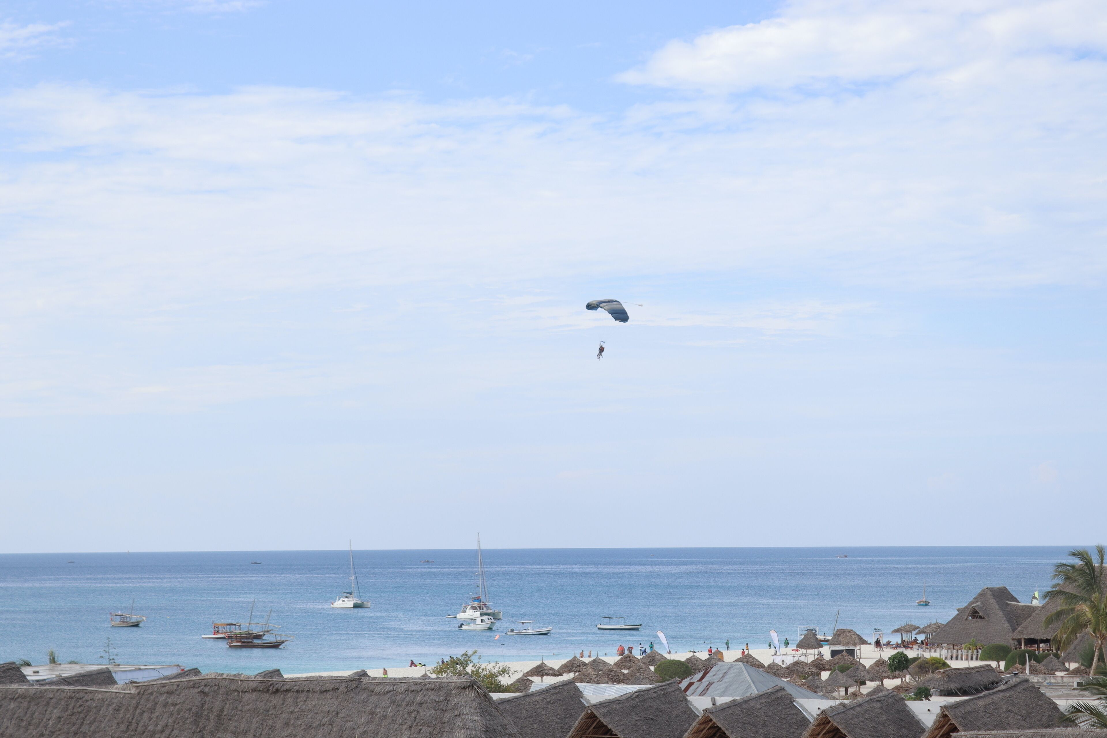 Uma praia com palafitas de telhado de palha, barcos na água e céu claro.