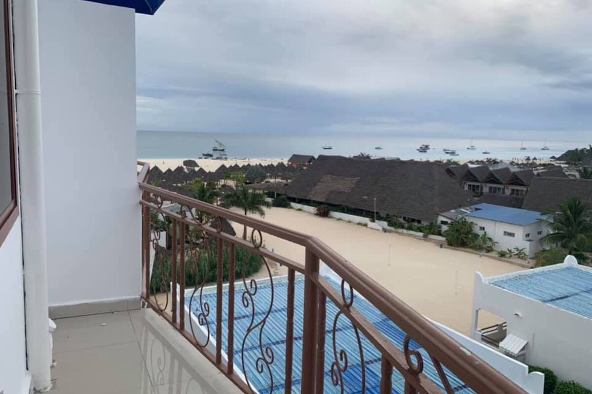 Un balcón con vistas a una playa, una piscina y varios edificios al fondo.