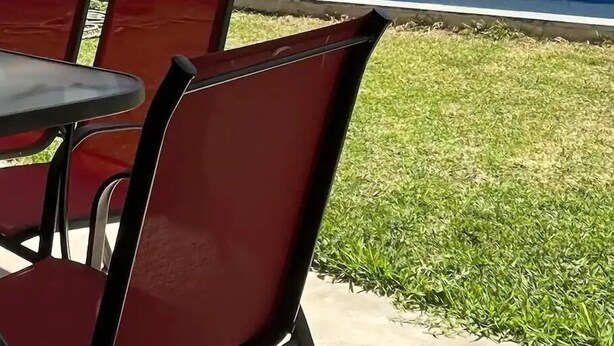 An outdoor seating area with red chairs and a table, a pool, and a white building with a lifebuoy on the wall. - Casa Arin (Mazatlán)