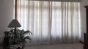 A room with a large window covered by sheer curtains, a floor lamp, and a potted plant. - Casa Arin (Mazatlán)