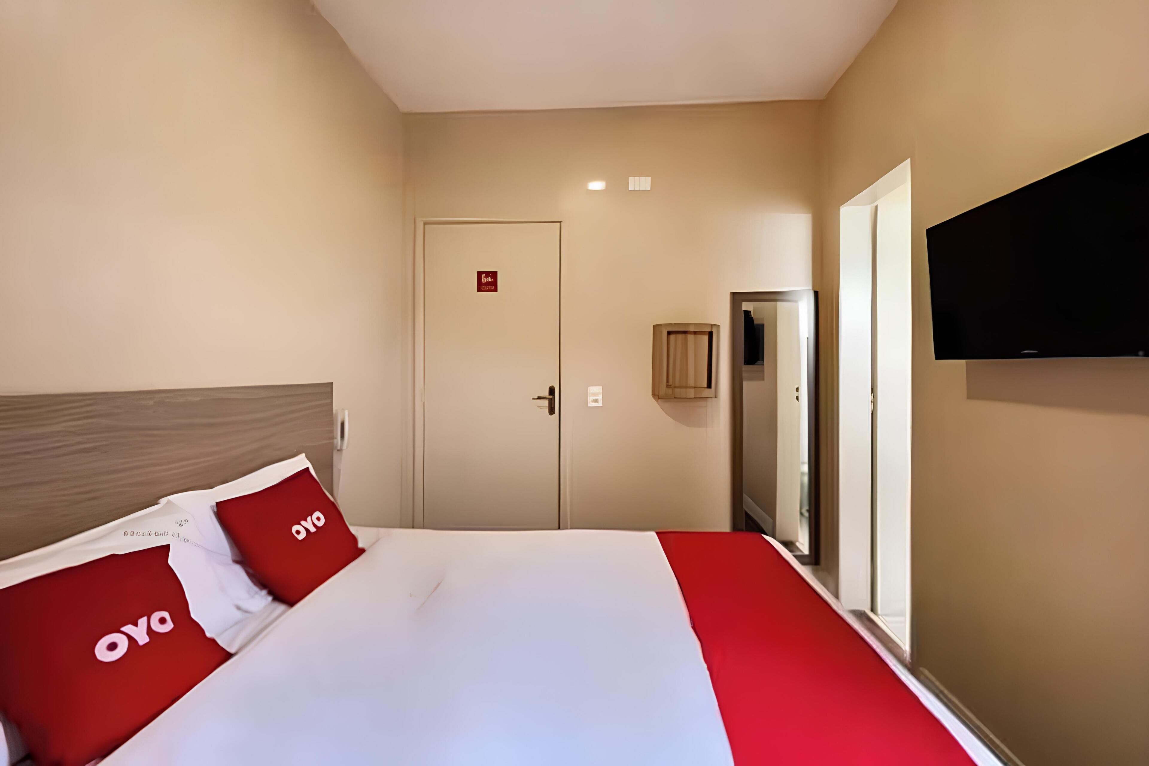 Une chambre d’hôtel avec un lit, un téléviseur fixé au mur et une porte avec une pancarte.