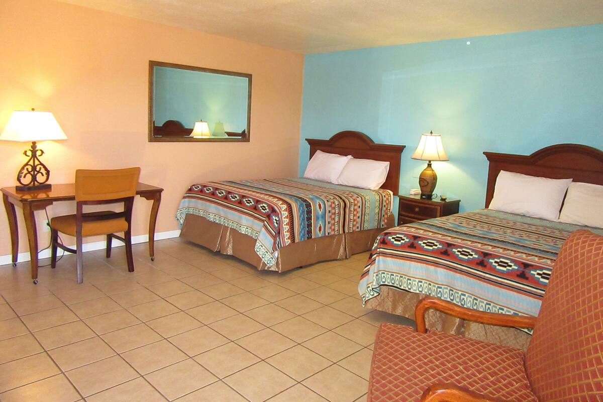 A hotel room with two beds, a desk, and a chair.