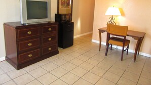 Una habitación de hotel con un aparador de madera, televisión, microondas, un cuadro enmarcado, una silla y una mesa.