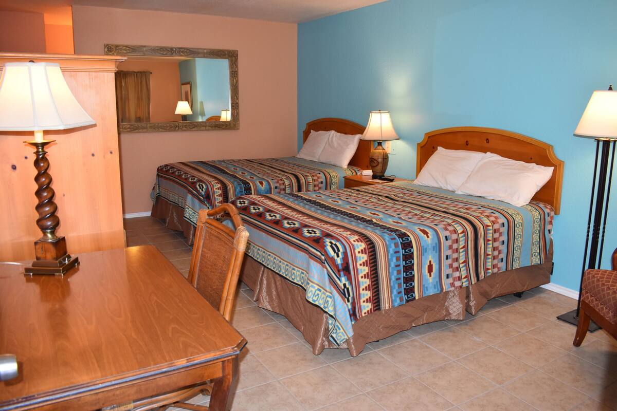 A hotel room with two beds, a wooden desk, a chair, a mirror, and two lamps.