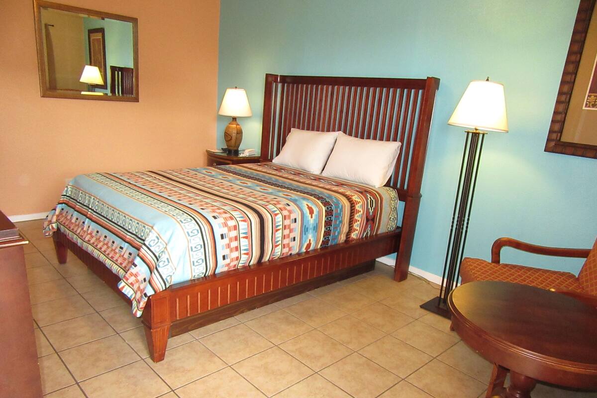 A bedroom with a wooden bed, two bedside lamps, a chair, and a mirror on the wall.