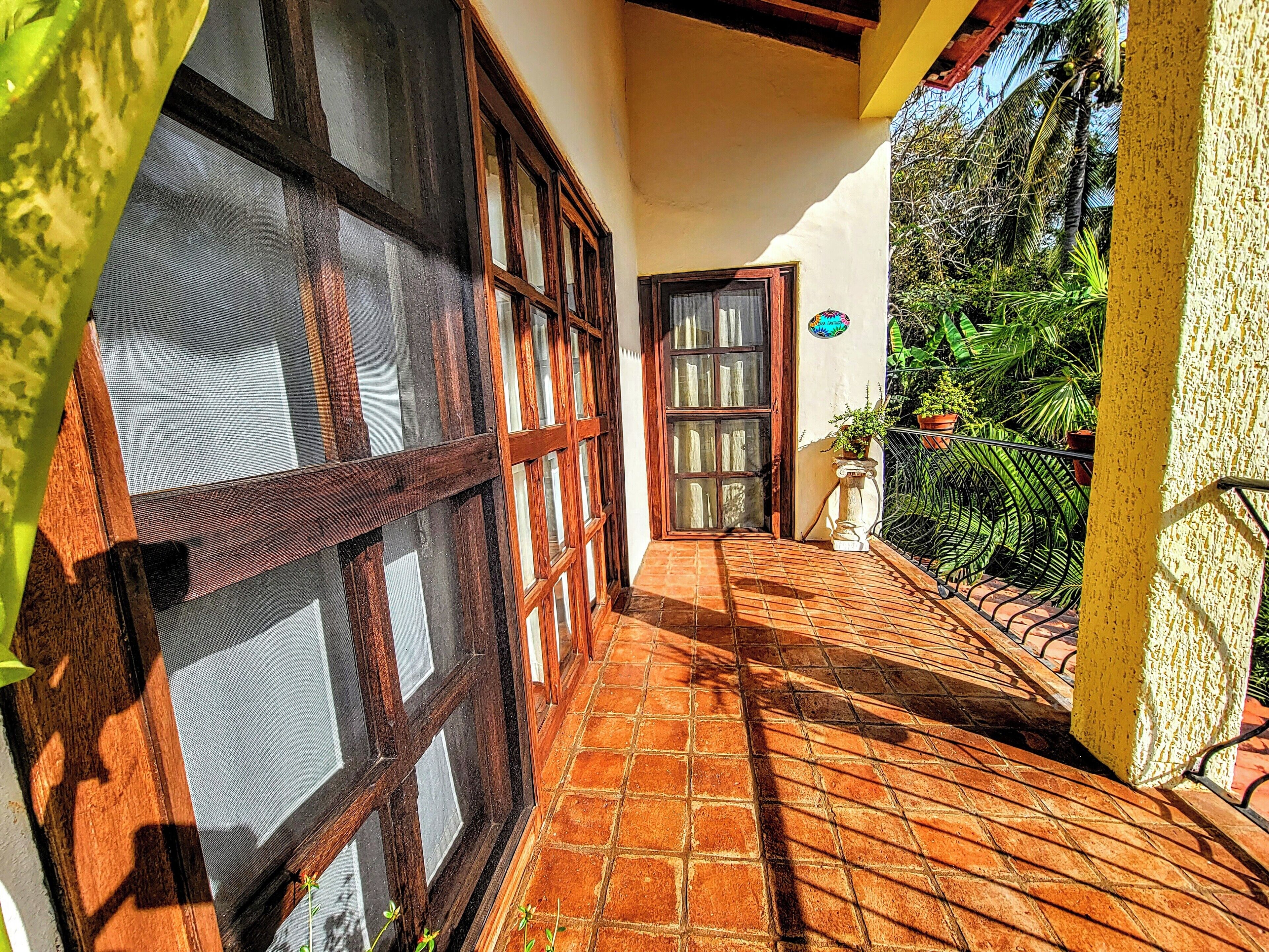 Un corredor estrecho con suelo de baldosas, una puerta de madera y una ventana con mosquitera.