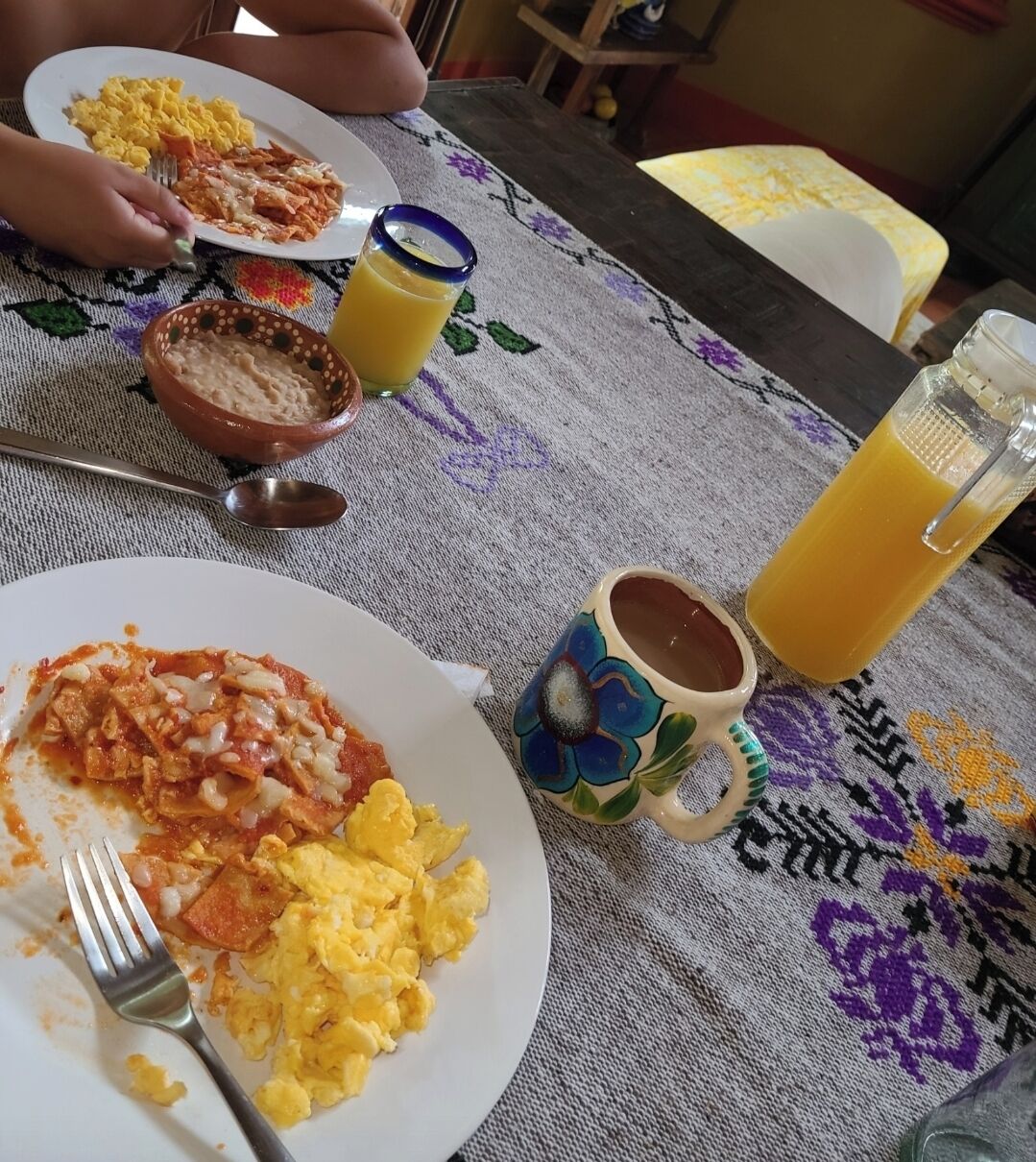 Une table à manger avec des assiettes remplies de nourriture, une tasse et un verre de jus d’orange.