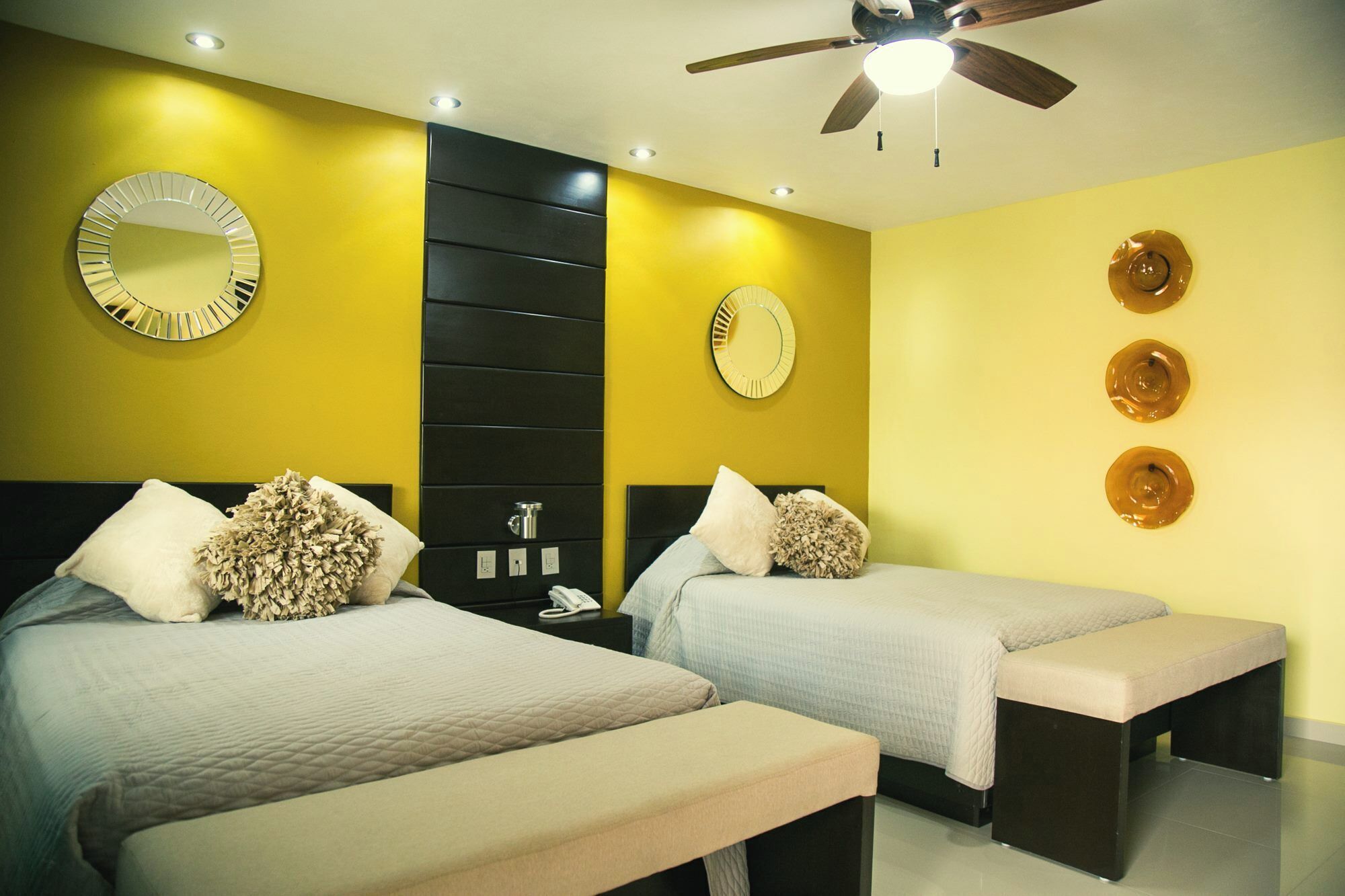 Habitación de hotel con dos camas, ventilador de techo y espejos decorativos en las paredes.
