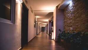 Um corredor comprido e estreito com piso de madeira, parede de pedra de um lado e uma porta no final.